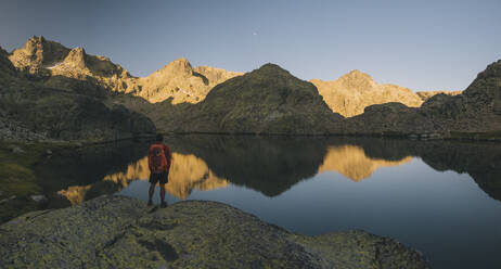 Ein junger Mann mit Rucksack betrachtet die Spiegelung im See, Sierra de Gredos - CAVF87808