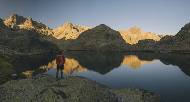 A young man with backpack looking at lake reflection, Sierra de Gredos - CAVF87808