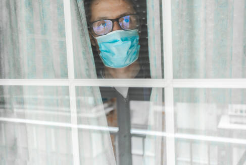 Middle-aged man in the medical mask is quarantined in the hospital and pressed her forehead against the window - CAVF87810