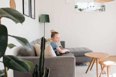 Young girl sat on the couch playing the guitar, at home - CAVF87825