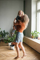 Woman holds in hugs her laughing child in living room with lot plants - CAVF87832