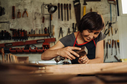 Holzarbeiterin bei der Arbeit in der Werkstatt, im Hintergrund hängen Werkzeuge - CAVF87857