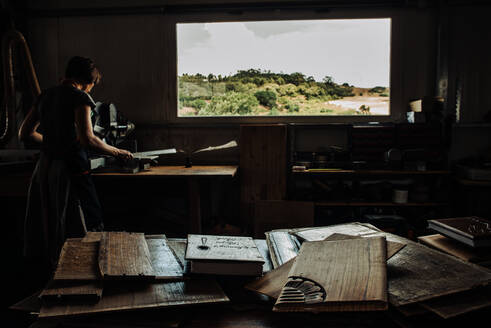 Frau bei der Arbeit in einer Werkstatt mit Holzplatten im Vordergrund, Low Key - CAVF87858