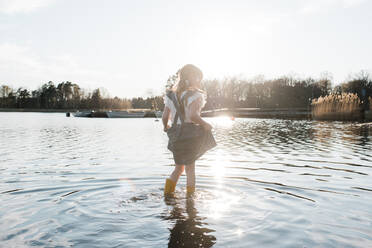 Young girl walking through the sea in a pretty dress at sunset - CAVF87862