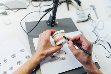 From above of crop anonymous dentistry student holding denture while training skills in modern laboratory - ADSF08765