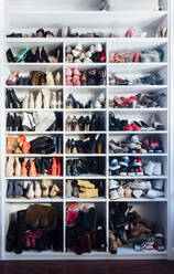 Modern white closet and square shelves with female colorful expensive high heels shoes and sneakers - ADSF08790