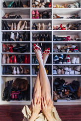 Crop female crossed legs in black tights and white high heel shoes with modern closet on background - ADSF08792