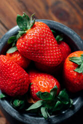 Frische reife Erdbeeren in schwarzer Betonschale auf Holzhintergrund - ADSF08821