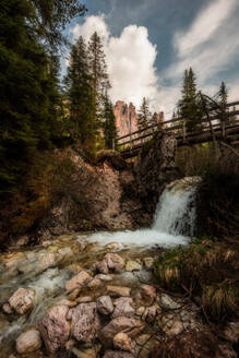 Rocky Boden mit schäumenden Strom von Wasser fließt unter hölzernen Brücke durch düstere Wald in den Bergen in bewölktem Tag in Dolomiten Italien - ADSF08833