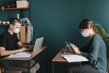 Young man and woman wearing protective masks working on desks at home - ALBF01313