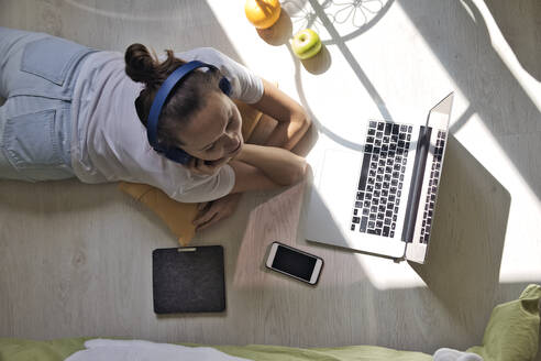 Junge Frau am Fenster liegend zu Hause mit Laptop - CAVF87921