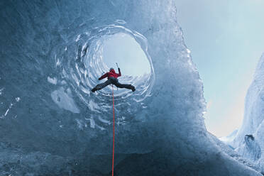 Woman climbing out of glacier cave / Sólheimajökull glacier in Iceland - CAVF87937