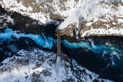 Luftaufnahme der Brücke über den Bruarfoss-Wasserfall mit kaskadenförmigem blauem Wasser, das durch die Winterlandschaft in Südisland fließt. - AAEF09227