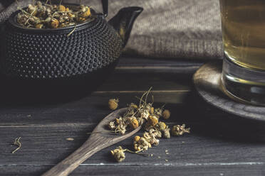 From above of dried daisy in spoon on dark wooden table near cup with herbal tea - ADSF08878