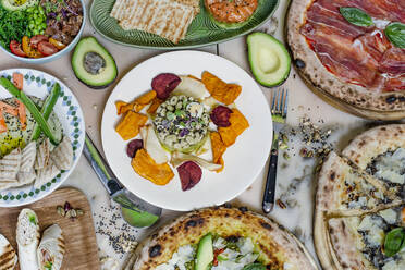 From above of dish of bean with petals on plate near fork with knife and pizza on table - ADSF08914