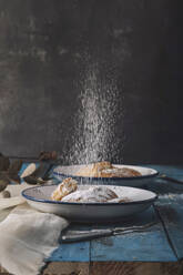 Puderzucker fällt in ein leckeres Dessert Brötchen auf blauem Tisch - ADSF08922