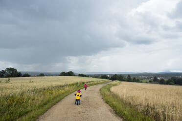 Mädchen mit Fahrrad und Balance-Fahrrad auf Feldweg, Regenwolken - BRF01482