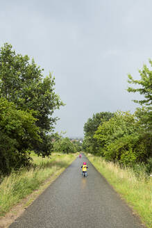 Mädchen mit Fahrrad und Gleichgewichtsfahrrad auf dem Fahrradweg bei Regenwetter - BRF01484