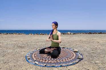 Woman practicing yoga and meditating at beach - MRRF00203