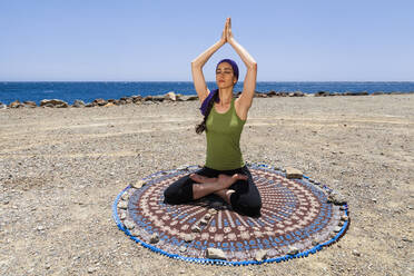 Woman practicing yoga and meditating at beach - MRRF00205