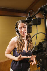 Singer with headphones at microphone in recording studio - LJF01734