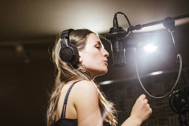 Singer with headphones at microphone in recording studio - LJF01744