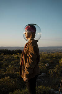 Woman with a fish bowl on her head in the countryside - RCPF00280