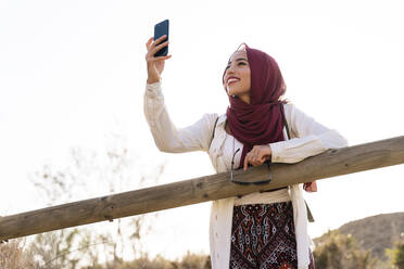 Lächelnde junge Touristin, die einen Hijab trägt und ein Selfie macht - MPPF00962