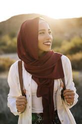 Lächelnde junge Touristin mit Hijab in Wüstenlandschaft, die sich umschaut - MPPF00975