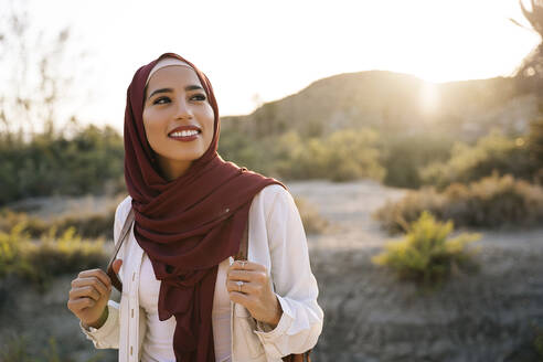 Lächelnde junge Touristin mit Hijab in Wüstenlandschaft, die sich umschaut - MPPF00976