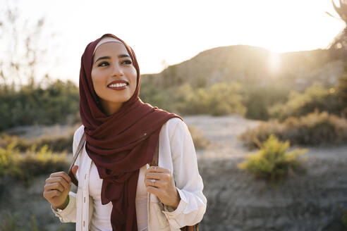 Smiling young tourist woman wearing Hijab in desert landscape looking around - MPPF00976
