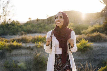 Lächelnde junge Touristin mit Hijab in Wüstenlandschaft, die sich umschaut - MPPF00977