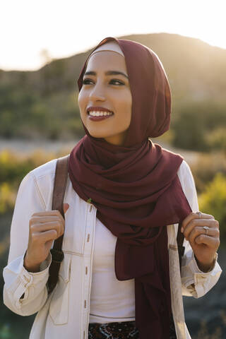 Lächelnde junge Touristin mit Hijab in Wüstenlandschaft, die sich umschaut, lizenzfreies Stockfoto