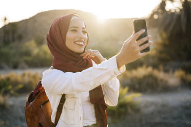 Lächelnde junge Touristin, die einen Hijab trägt und ein Selfie macht - MPPF00979