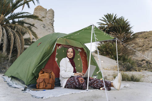 Young woman wearing Hijab using laptop at a tent - MPPF00993