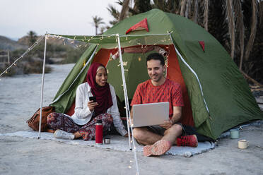 Young woman wearing Hijab and man using laptop at a tent - MPPF01000