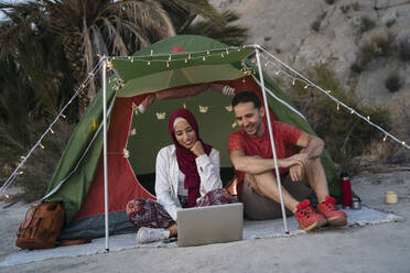 Young woman wearing Hijab and man using laptop at a tent - MPPF01001