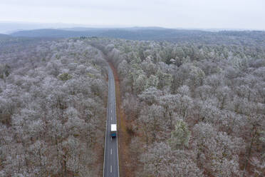 Deutschland, Bayern, Drone view of truck driving along asphalt road cutting through Steigerwald in winter - RUEF03015