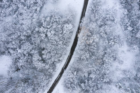 Drohnenansicht einer asphaltierten Straße, die sich durch einen verschneiten Wald in der Frankenhöhe schlängelt - RUEF03034