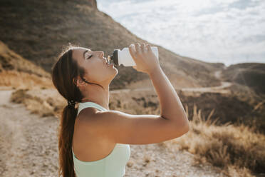 Athlete woman drinking water from a bottle in the mountains - MIMFF00128