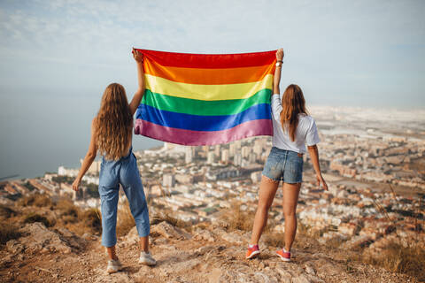 Zwei junge Frauen mit einer LGBT-Flagge über der Küstenstadt Almeria, Spanien, lizenzfreies Stockfoto