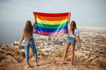 Two young women with an LGBT flag above the coastal city of Almeria, Spain - MIMFF00129
