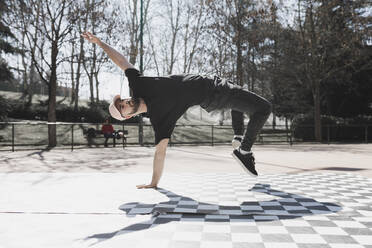 Young athletic guy practicing break dance in park in sunny weather - ADSF08950