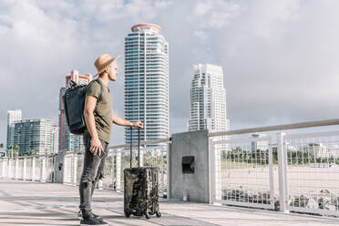 https://us.images.westend61.de/0001433218j/young-man-standing-with-suitcase-and-enjoying-the-view-before-departure-outdoors-skyscraper-background-ADSF09099.jpg