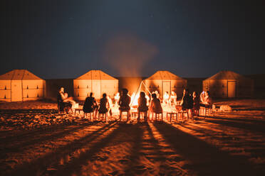 Gruppe von Reisenden sitzen um brennende helle Lagerfeuer auf Sand in der Wüste mit Zelten, Marokko - ADSF09129