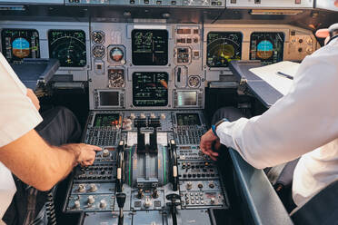 Back view of crop anonymous male captain and pilot sitting in cockpit of modern airplane and checking equipment while preparing for departure - ADSF09159