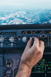 Rückenansicht eines anonymen männlichen Piloten, der während eines Fluges über felsigem Gelände einen Schalter am Bedienfeld im Cockpit umlegt - ADSF09163