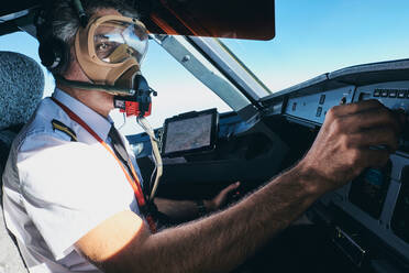 Seitenansicht eines professionellen männlichen Fliegers mit Sauerstoffmaske, der einen Schalter an der Steuerkonsole umlegt, während er ein modernes Flugzeug während des Fluges bedient - ADSF09165