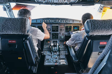 Back view of male pilot and co pilot using instrument panel in cockpit of modern passenger aircraft during flight - ADSF09174