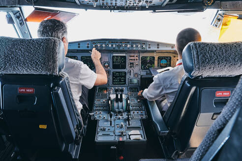 Rückenansicht eines männlichen Piloten und eines Co-Piloten, die das Instrumentenbrett im Cockpit eines modernen Passagierflugzeugs während des Fluges benutzen - ADSF09174